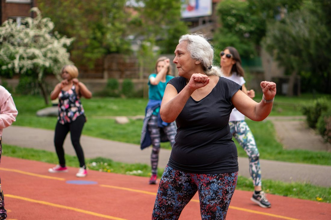 An older participant takes part in an outdoor FITCare fitness class with other group members behind her