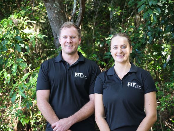 Male and female FIT Care support workers standing infront of a background of tress.